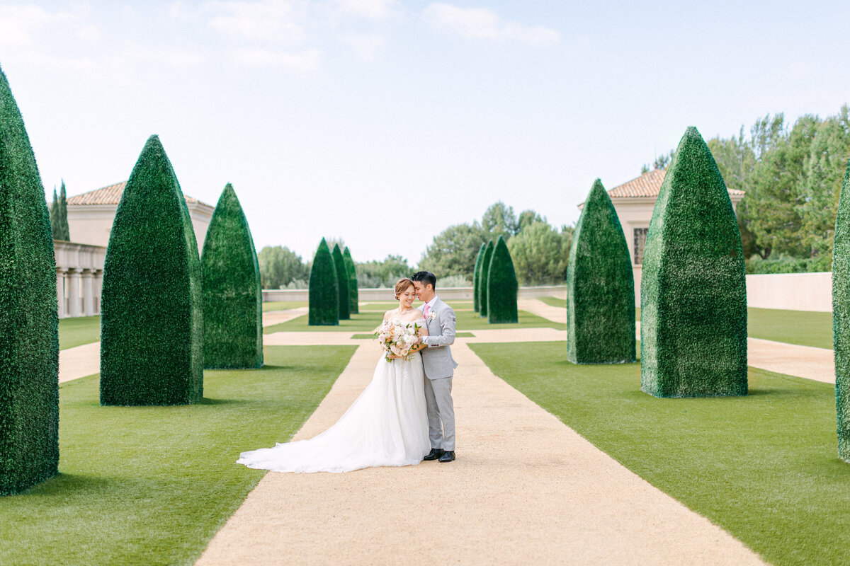 Bride and groom hand in hand between towering topiary hedges