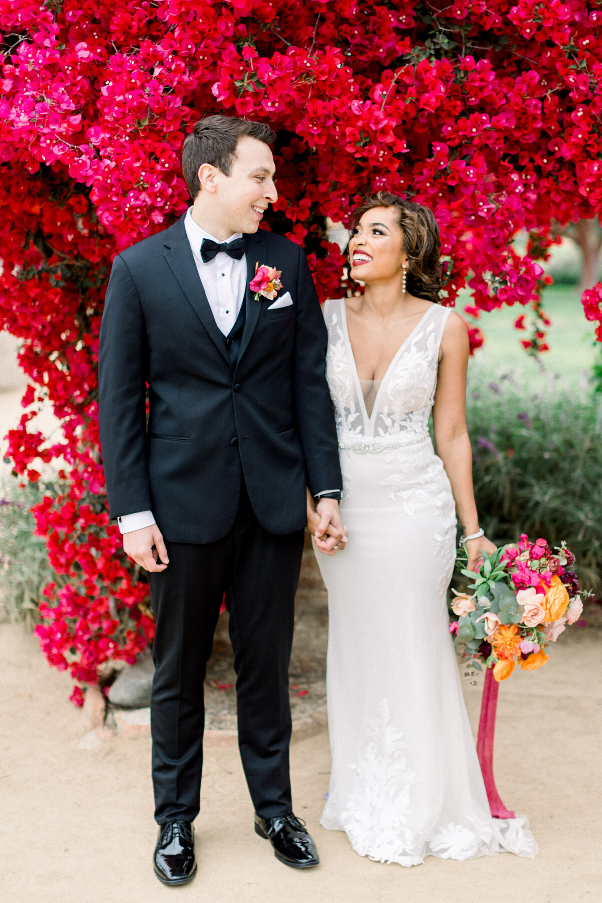 Bride and groom laughing beneath a wall of pink bougainvillea