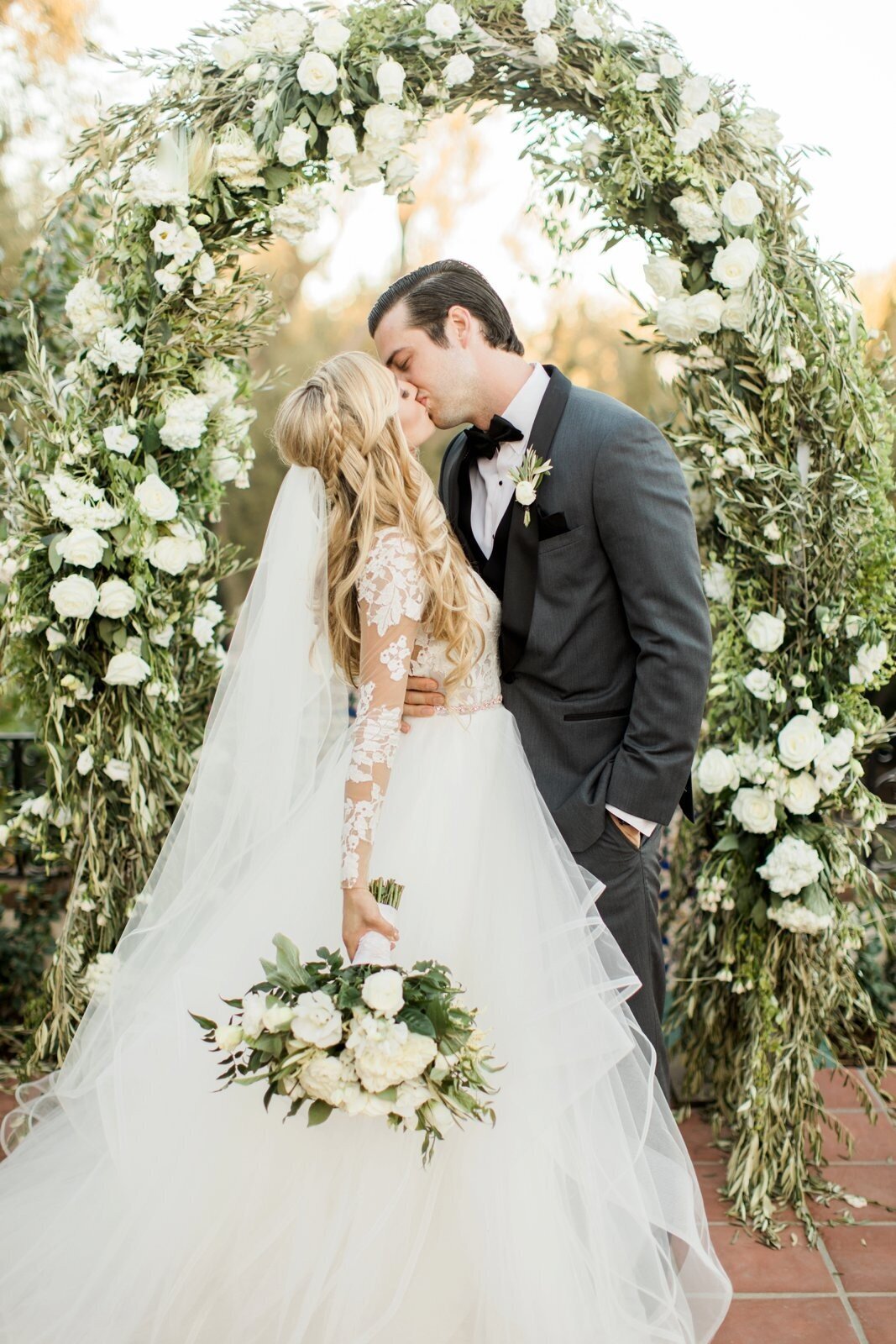Bride and groom framed by a sweeping greenery arch