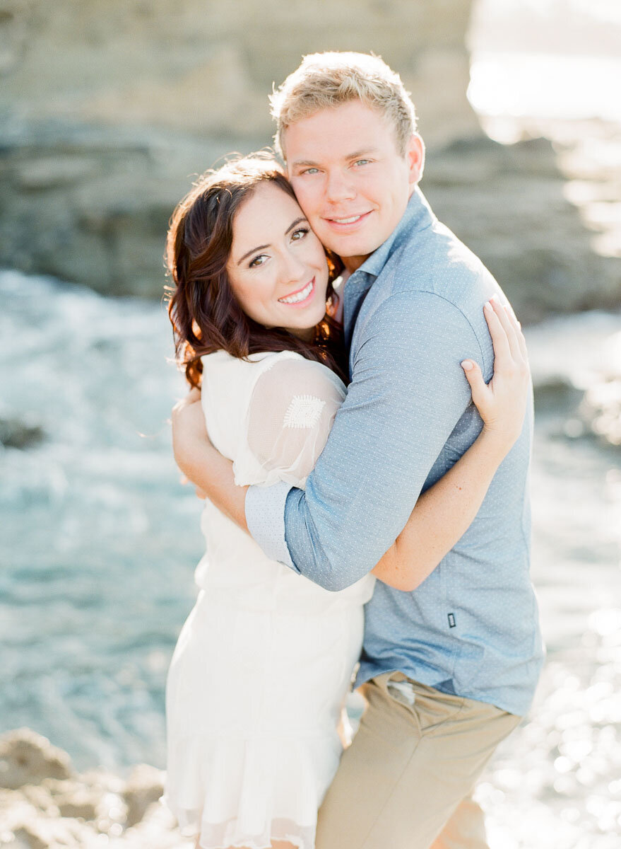Engaged couple embracing on the rocks above the sea