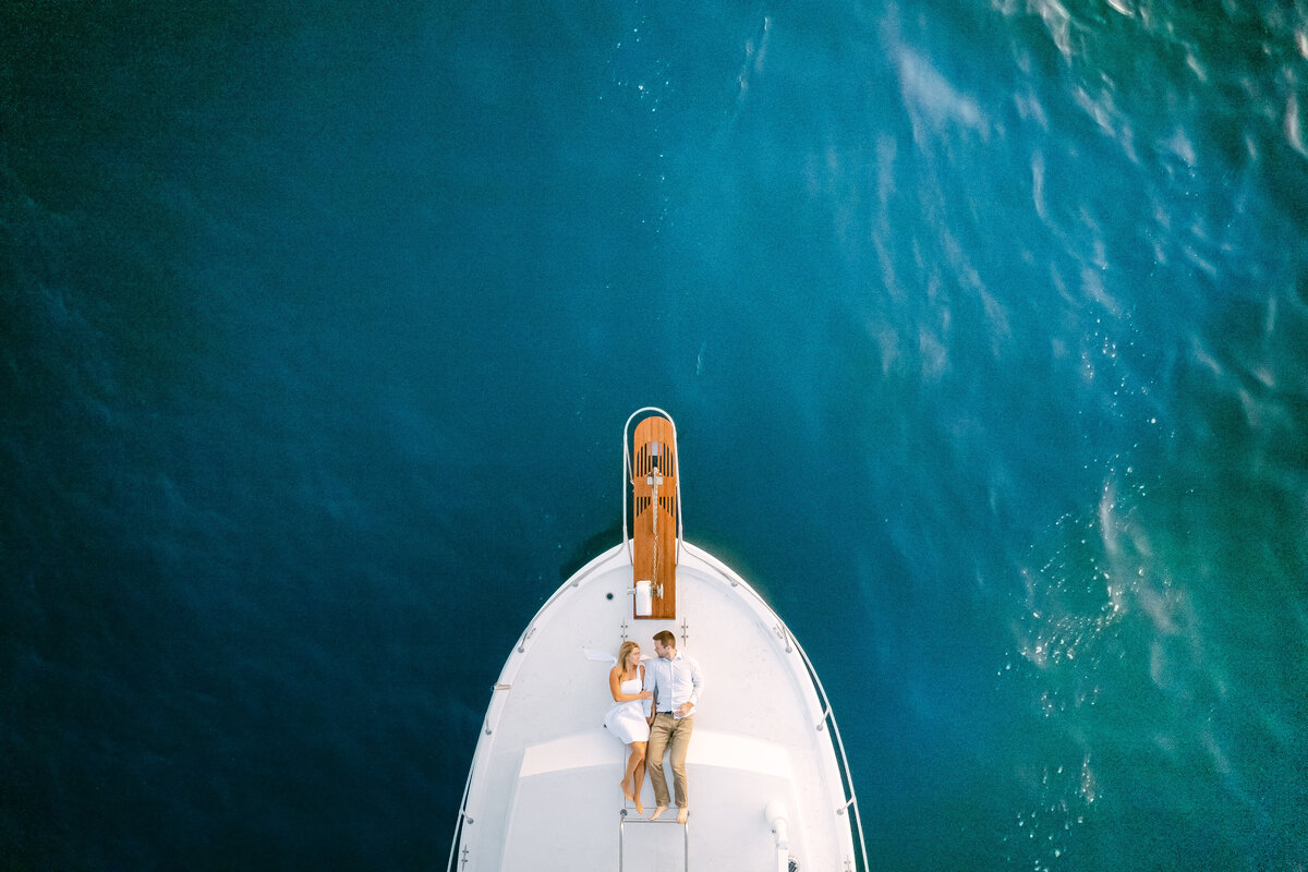 Aerial photograph of a couple on a yacht bow over teal water