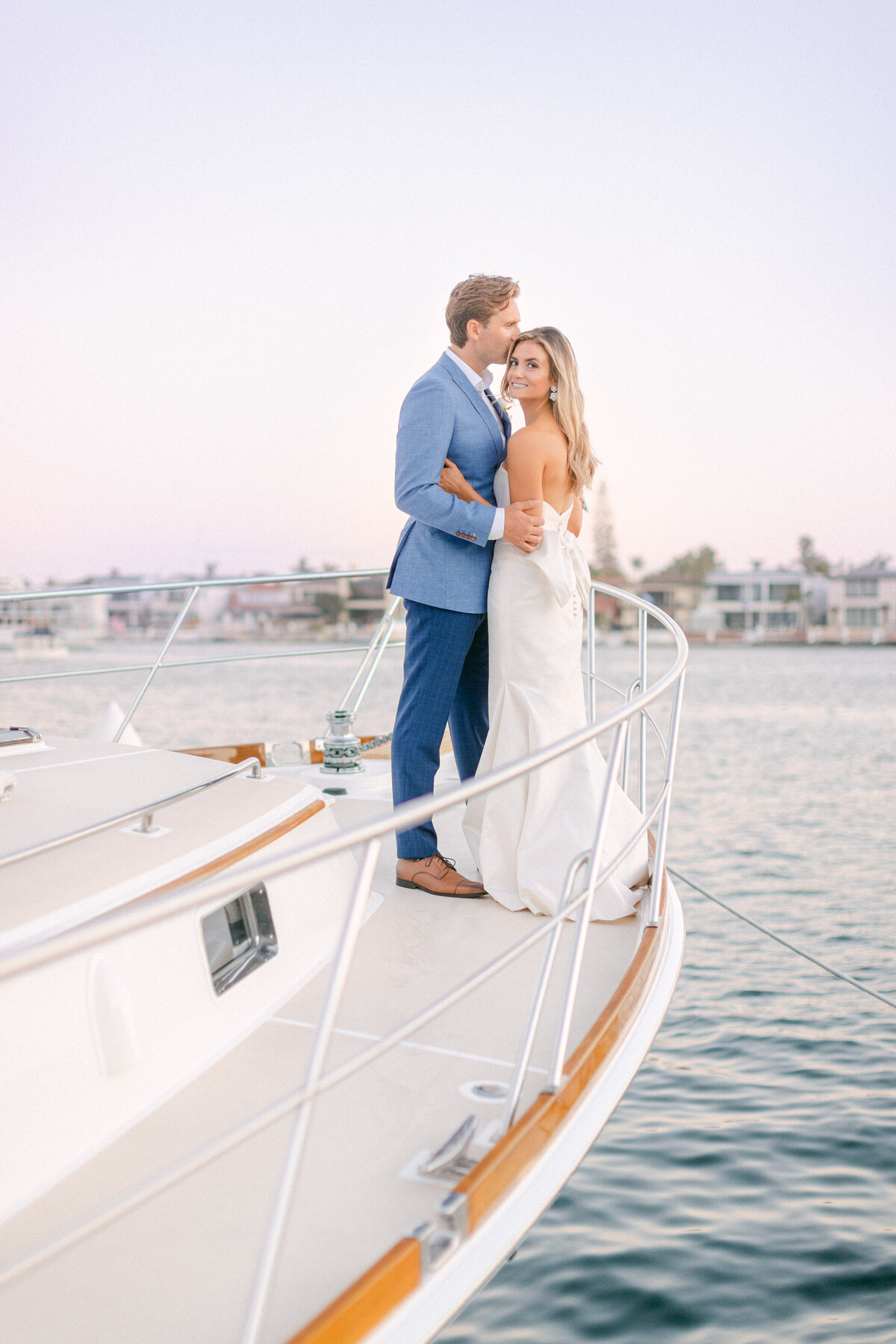 Bride and groom on the bow of a classic yacht in Newport Harbor at dusk