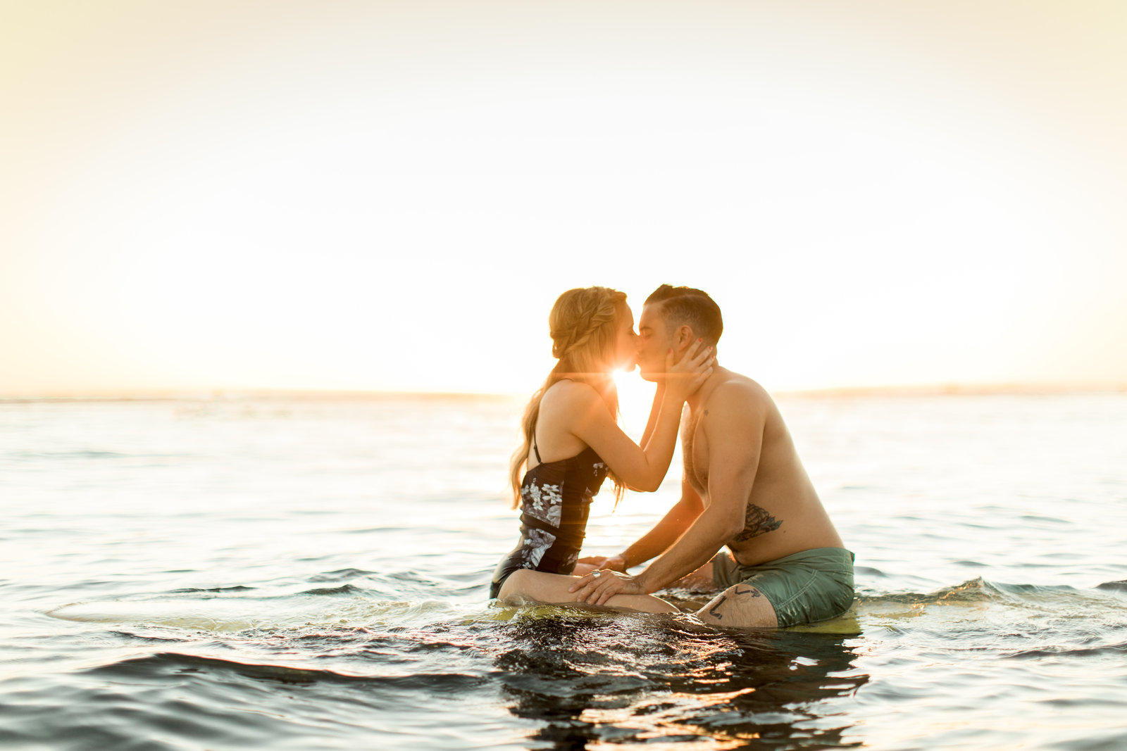 Couple kissing on a surfboard in the water at sunset off San Clemente