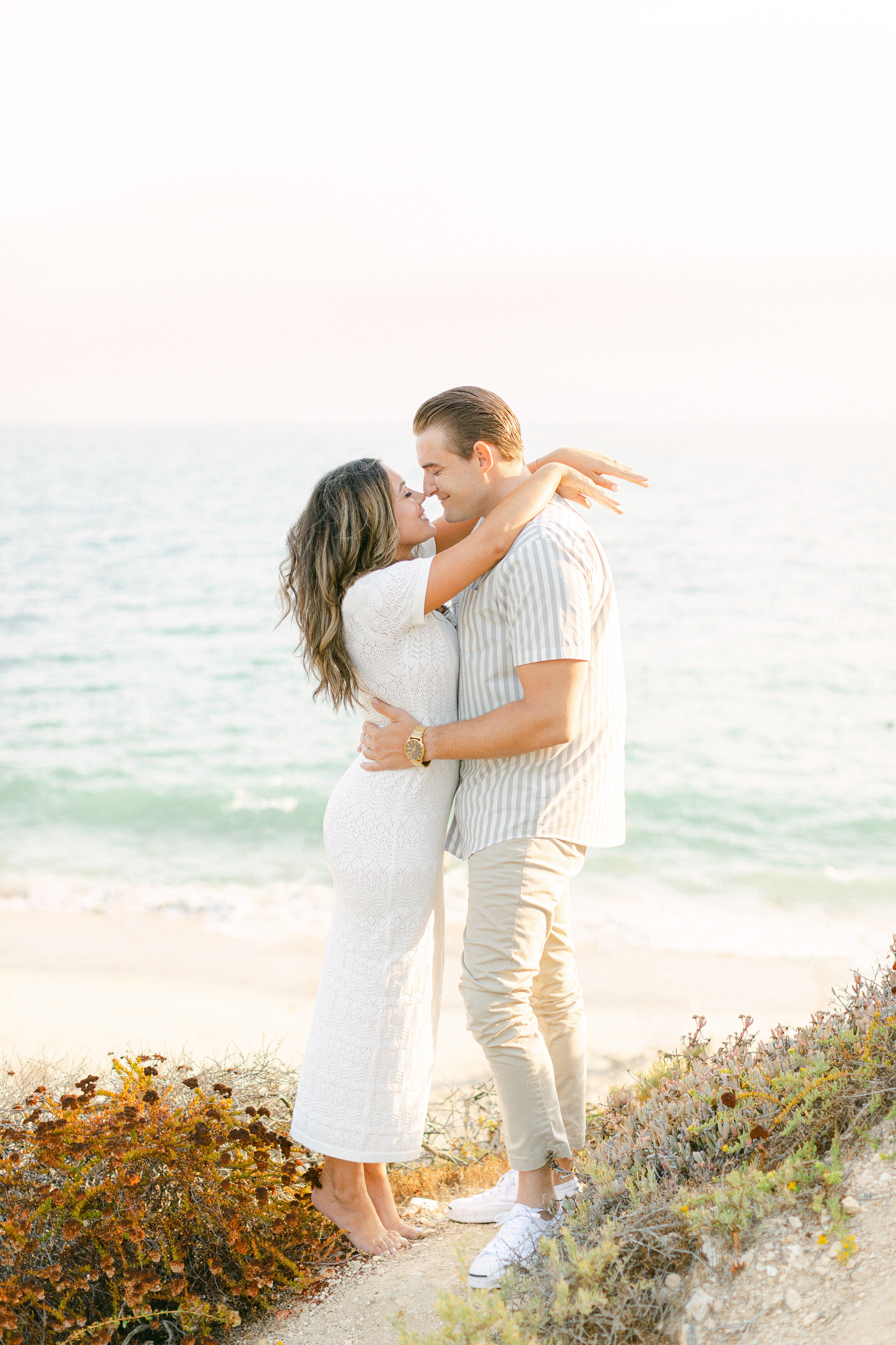 Couple embracing on a coastal bluff above the Pacific at golden hour